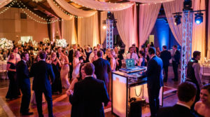 Un DJ avec casque mixe de la musique pour des invités qui dansent sur une piste éclairée lors d'une réception de mariage.