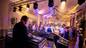 Un DJ avec un casque aux platines, mixant pour des invités de mariage dansant dans une salle de réception festive.