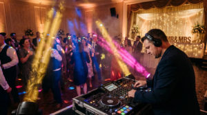 DJ en action à un mariage, avec des lumières vives et des invités dansant joyeusement sur la piste de danse. Signe 'Mr & Mrs' visible.