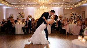 Mariés souriants dansent, le marié faisant pencher la mariée en arrière. Ambiance chaleureuse avec lumières et invités.